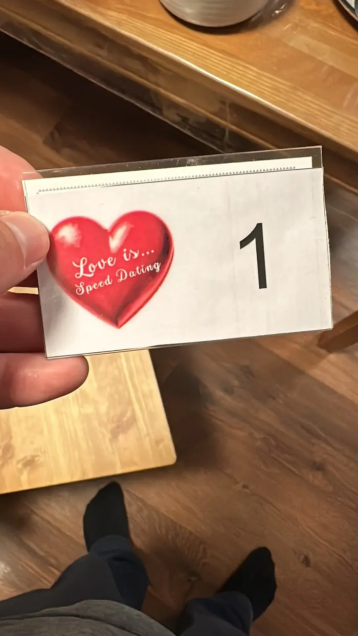 Бейдж участника с номером 1 и знаком «Love is… Speed Dating» в руке.