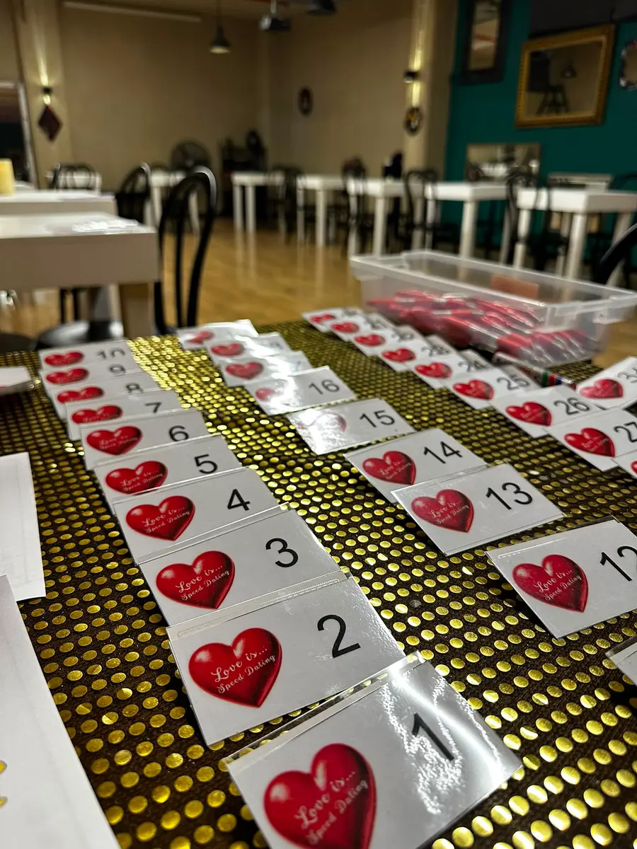 Пронумерованные бейджи с красным сердцем «Love is… Speed Dating» разложены на столе перед началом вечера.
